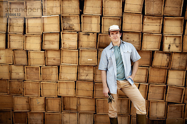 Ein Landwirt steht vor einer Wand aus gestapelten Holzkisten für die Produktion.