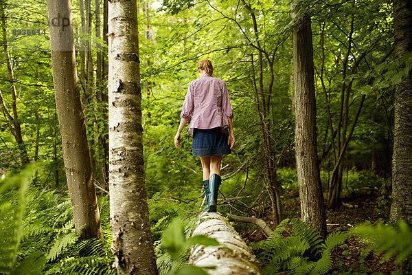 Eine Frau in Gummistiefeln  die an einem umgefallenen Baumstamm entlang geht  im Wald.