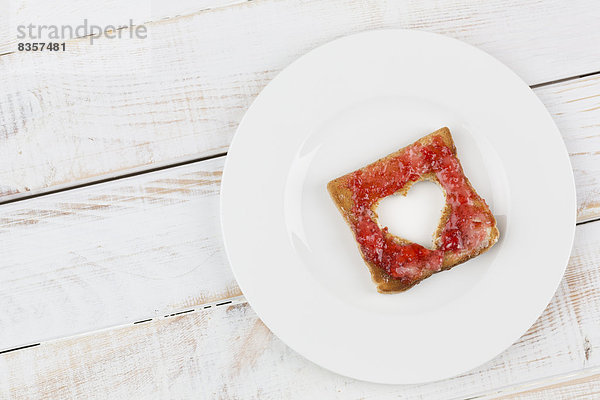 Toast mit roter Marmelade und herzförmigem Loch auf Teller  Studioaufnahme