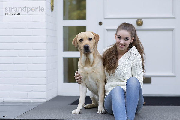 Teenagermädchen mit Hund vor einer Haustür sitzend