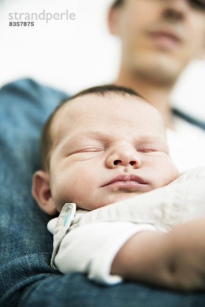 Junger Vater hält seinen schlafenden  neugeborenen Sohn in der Hand