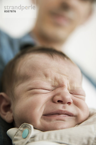 Junger Vater hält seinen weinenden  neugeborenen Sohn.