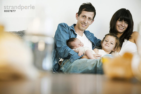 Junge Familie mit männlichem Neugeborenen und kleiner Tochter  die zu Hause auf dem Sofa sitzt.