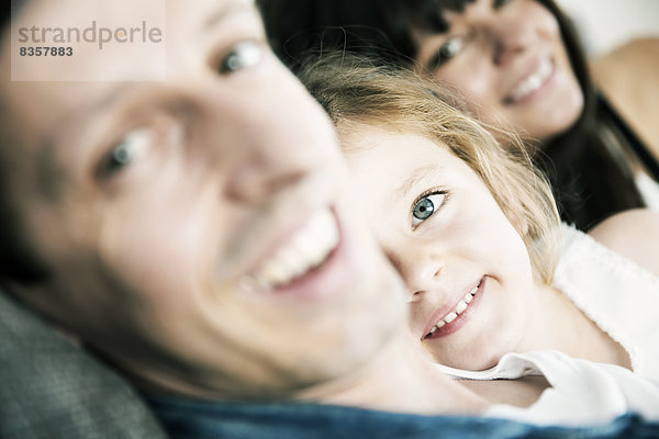 Lächelnde junge Eltern mit kleiner Tochter auf dem Sofa zu Hause  Nahaufnahme