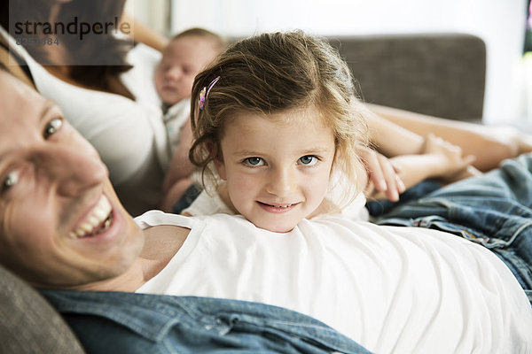 Junge Eltern mit männlichem Neugeborenen und kleiner Tochter  die zu Hause auf dem Sofa sitzt.