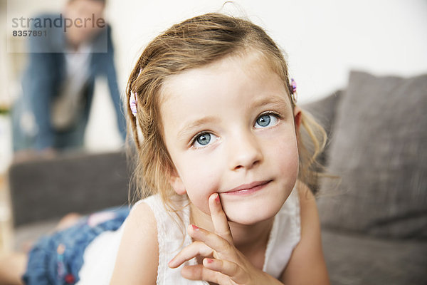 Porträt eines kleinen Mädchens auf dem Sofa  ihr Vater im Hintergrund stehend