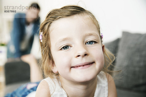 Porträt eines lächelnden jungen Mädchens auf dem Sofa  ihr Vater im Hintergrund stehend