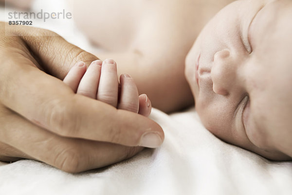 Mutter hält die Hand ihres schlafenden  neugeborenen Sohnes.