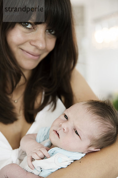 Lächelnde junge Mutter mit ihrem neugeborenen Sohn im Arm