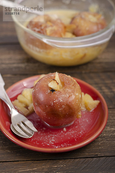 Baked apples with almonds  gloves and cinnamon in glass bowl and red plate on wooden table  studio shot