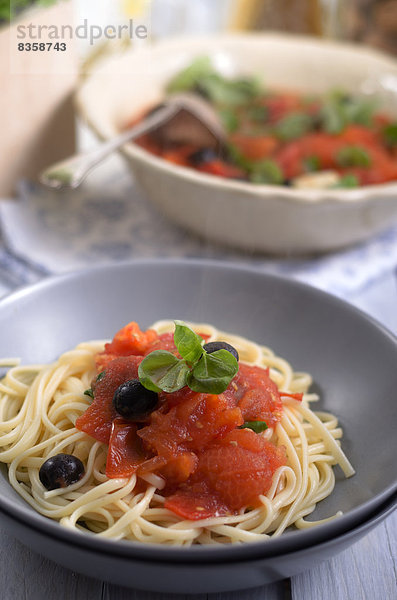 Spaghetti with sauce made of grilled tomatoes with black olives and leaves of basil  studio shot