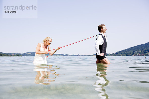 Germany  Bavaria  Tegernsee  Wedding couple standing in lake  bride holding groom on leash