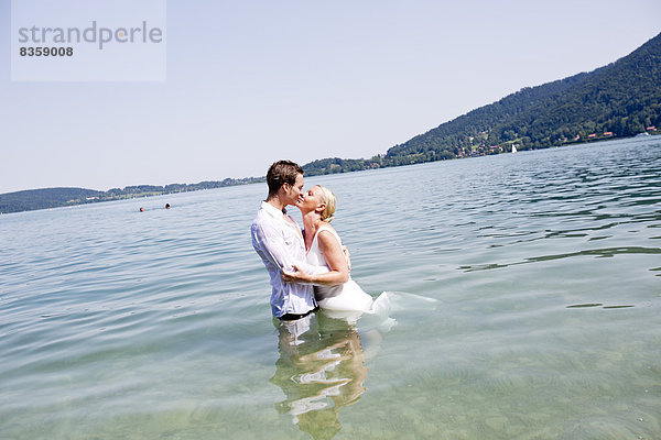 Germany  Bavaria  Tegernsee  Wedding couple standing in lake  kissing