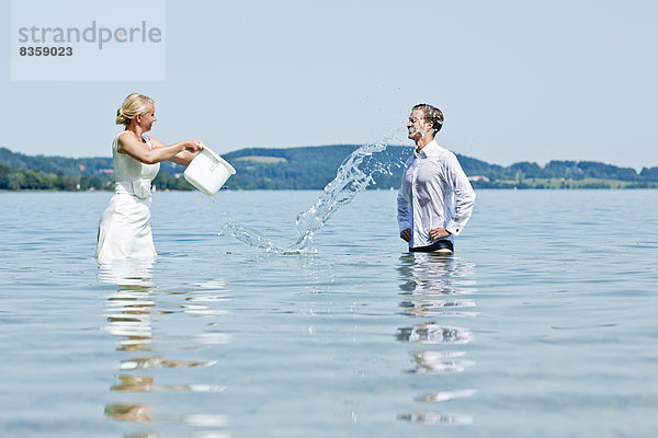 Deutschland  Bayern  Tegernsee  Hochzeitspaar im See stehend  Wasser über den Bräutigam gießend