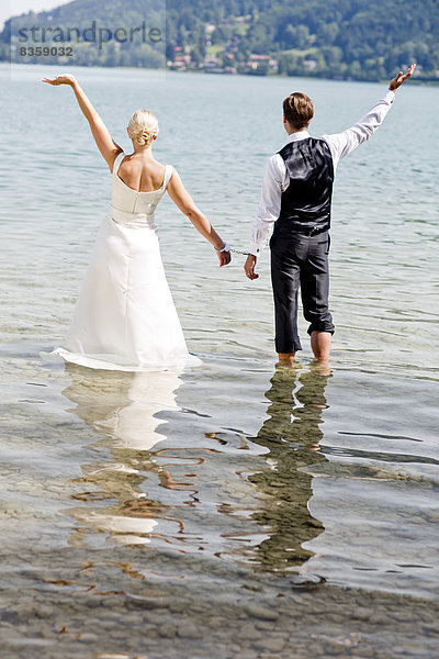 Deutschland  Bayern  Tegernsee  Hochzeitspaar im See stehend mit Handschellen