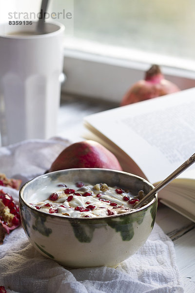 Healthy breakfast with pomegranate in yogurt  coffee and opened book