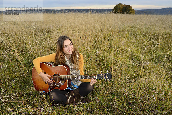 Lächelnde junge Frau spielt Gitarre auf einem Feld