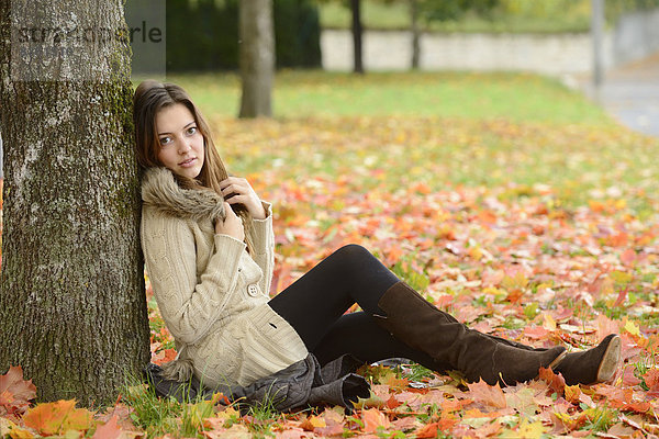 Junge Frau sitzt unter einem Baum im Herbst