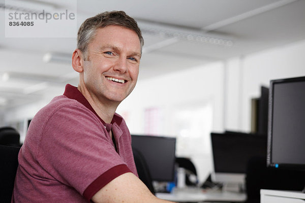 Mann am Schreibtisch sitzend mit Computer  lächelnd vor der Kamera