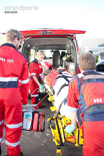 Rettungssanitäter heben Frau auf Trage in den Krankenwagen