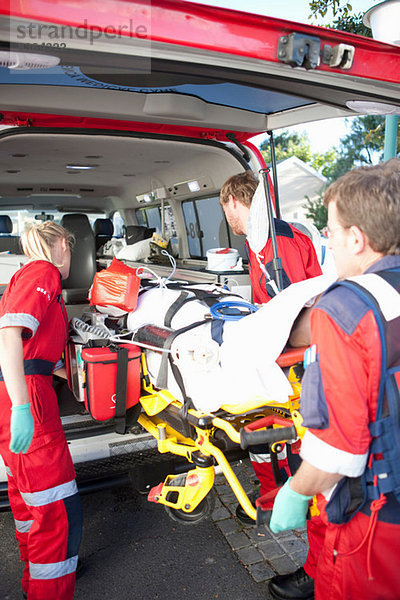 Rettungssanitäter heben Frau auf Trage in den Krankenwagen