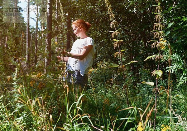 Frau steht im Wald und schaut auf Pflanzen