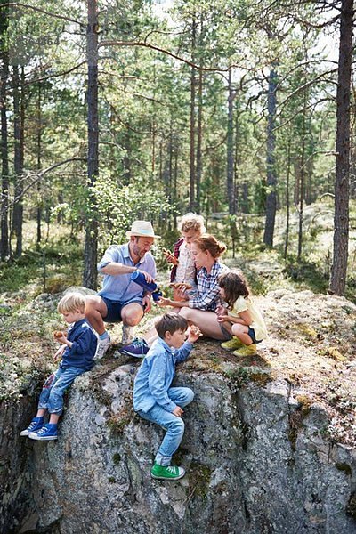 Familie sitzt auf Felsen im Wald und isst Picknick
