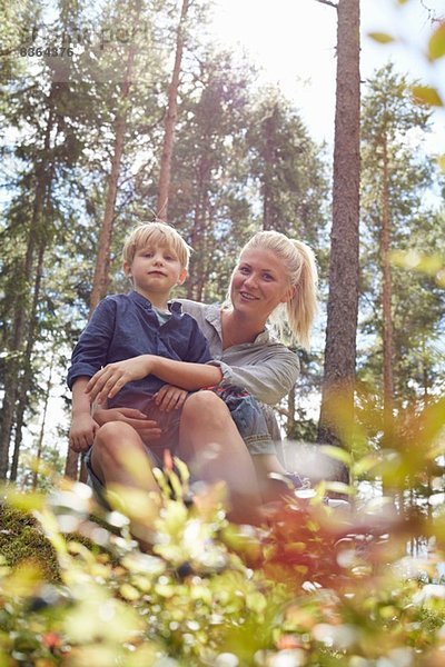 Junge auf dem Schoß der Mutter im Wald sitzend
