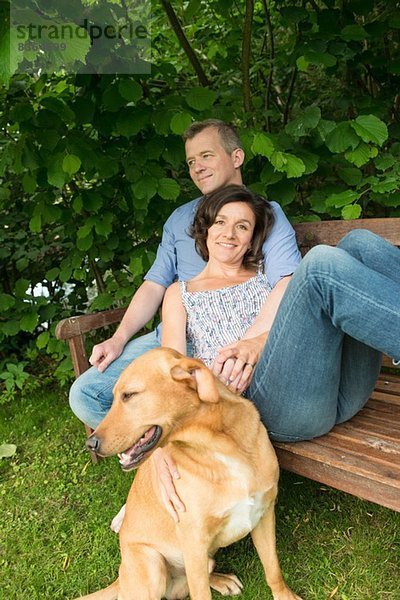Erwachsenes Paar sitzt auf einer Gartenbank mit Hund