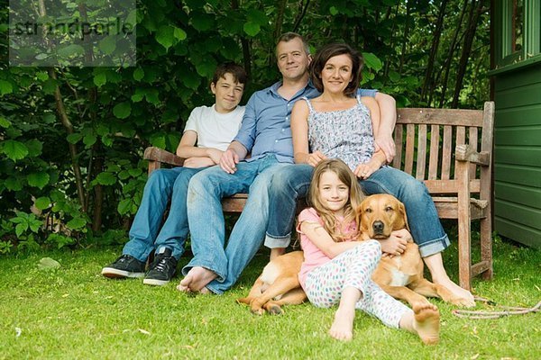 Porträt einer Familie mit zwei Kindern auf einer Gartenbank mit Hund