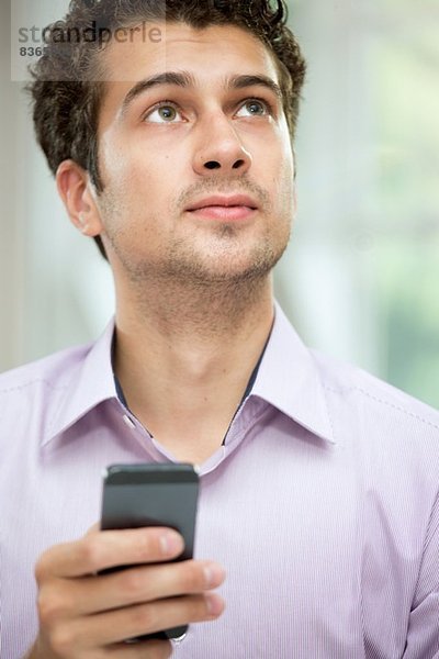 Junger Mann schaut vom Handy auf.