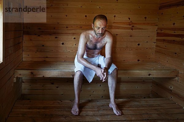 Der reife Mann entspannt sich in der Sauna mit dem Kopf nach unten.