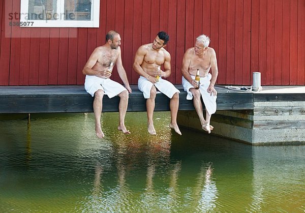 Drei männliche Freunde bei einem Bier vor der Sauna