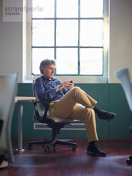 Erwachsener Geschäftsmann sitzt auf Bürostuhl mit Handy