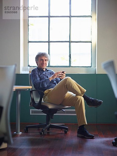 Erwachsener Geschäftsmann sitzt auf Bürostuhl mit Handy