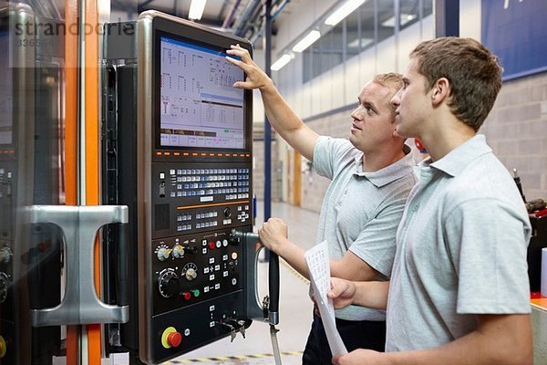 Arbeiter  die den Computerbildschirm in der Maschinenfabrik betrachten