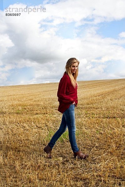 Porträt einer jungen Frau  die auf einem geernteten Feld spazieren geht.