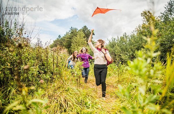 Vier junge Frauen laufen mit dem Drachen durchs Buschland