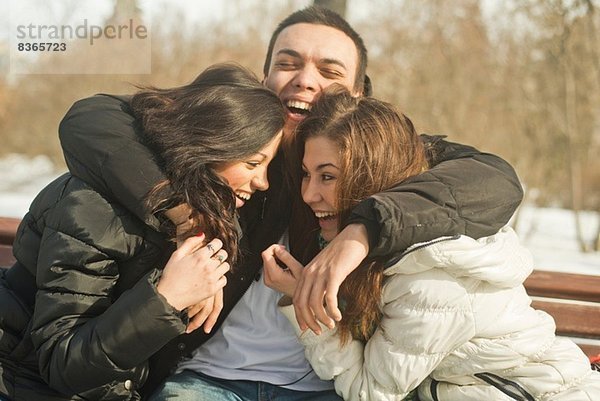 Drei junge Erwachsene  die sich im Winter auf der Parkbank umarmen
