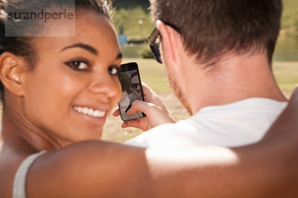 Junges Paar fotografiert sich mit Telefon  Frau schaut über die Schulter