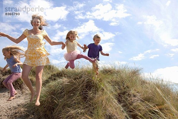 Mutter mit drei Kindern  die von den Dünen springen  Wales  UK