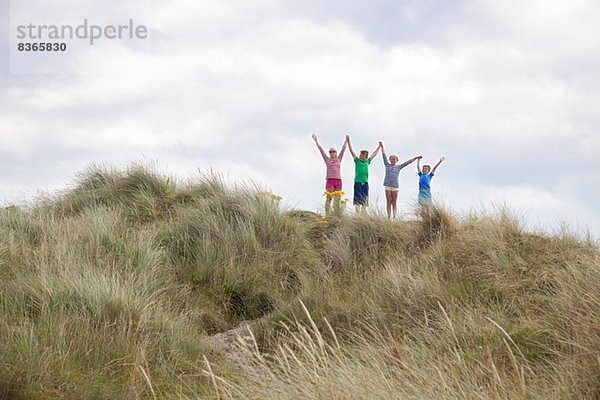 Vier Freunde auf Dünen mit ausgestreckten Armen  Wales  UK