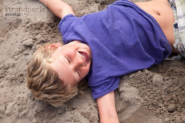 Junge auf Sand liegend lachend  Wales  UK