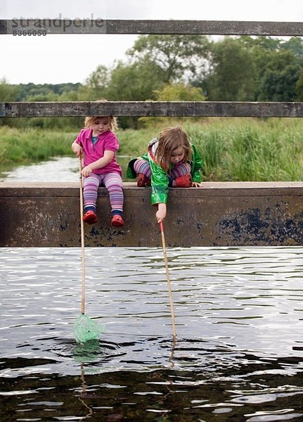 Zwei Mädchen sitzen auf einer Brücke mit Fischernetzen  Amersham  Buckinghamshire  England  UK