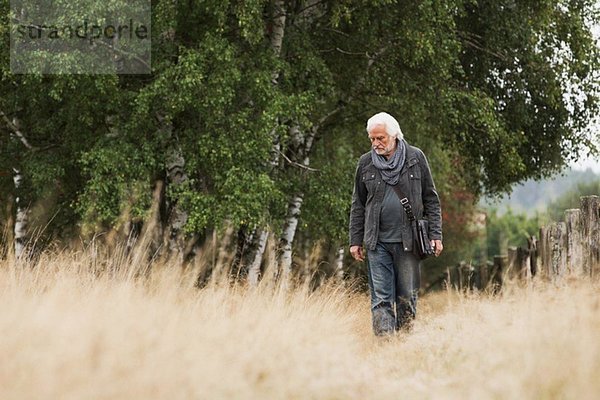 Älterer Mann  der auf der Wiese spazieren geht.