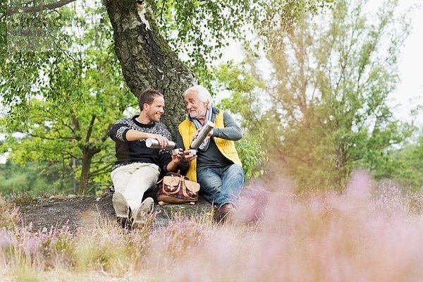 Vater und erwachsener Sohn trinken Kaffee aus der Flasche