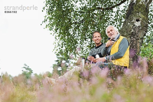 Vater und erwachsener Sohn trinken Kaffee aus der Flasche