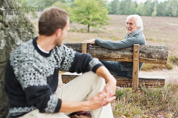 Älterer Mann sitzt auf der Bank und redet mit einem erwachsenen Mann.