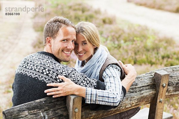 Mittleres erwachsenes Paar auf Holzbank mit Blick auf die Kamera