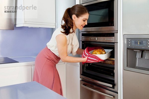 Junge Frau nimmt Bratschüssel aus dem Ofen